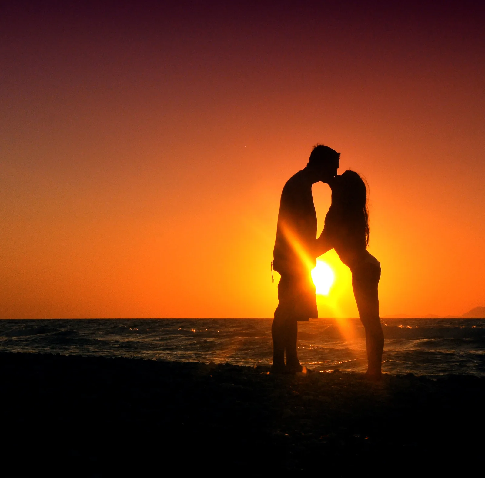 Silueta de una pareja besándose frente al atardecer en la playa