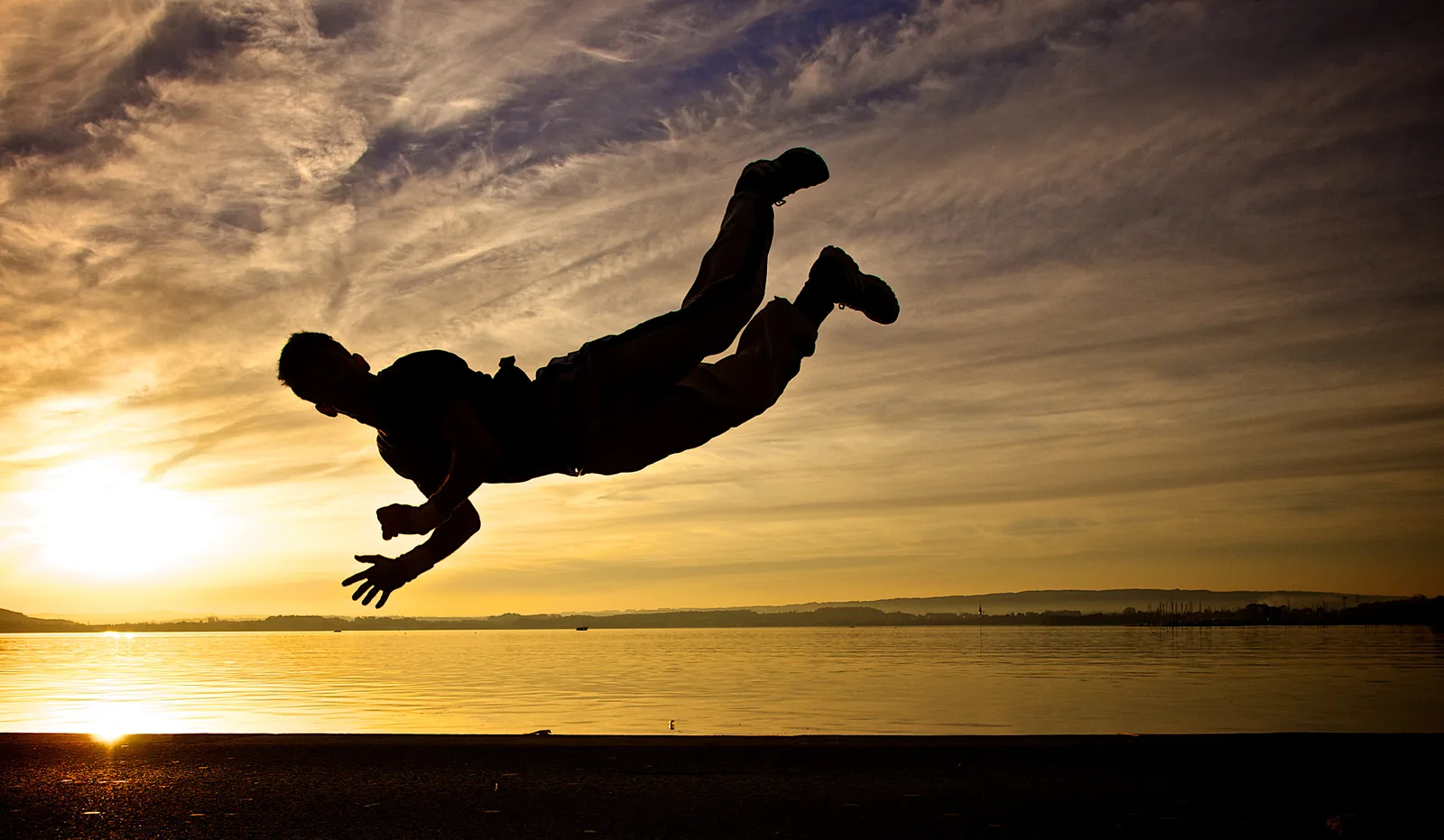 Silueta de una persona bailando frente a un atardecer junto al agua