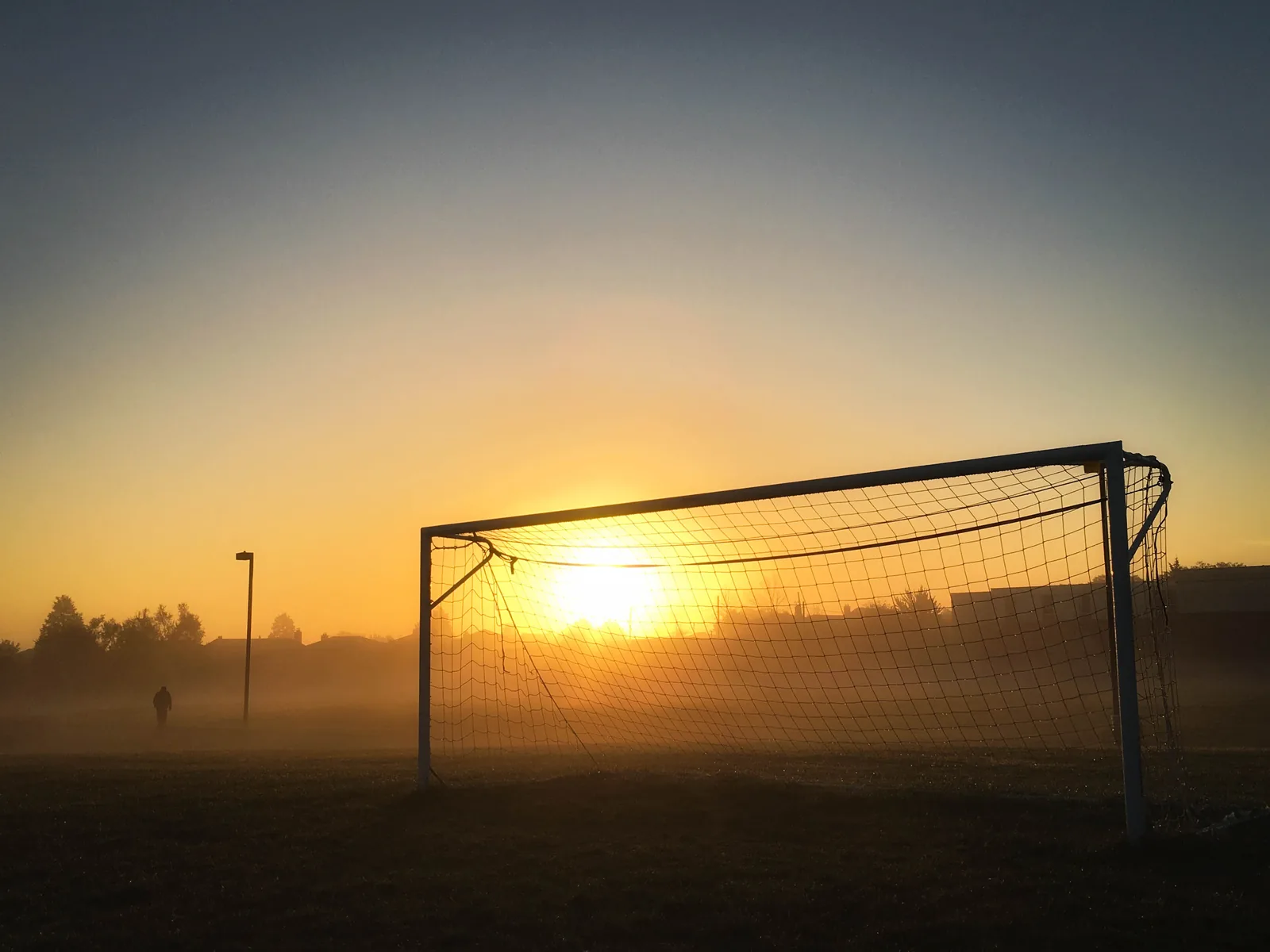 Arco de fútbol vacío al amanecer, con niebla sobre el campo