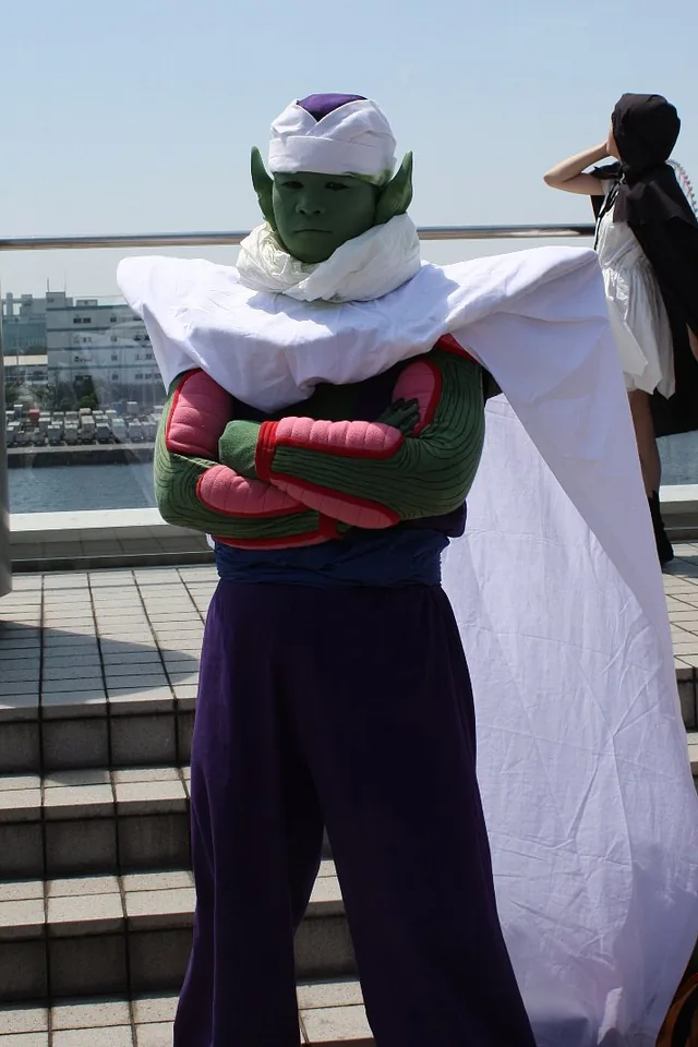 Cosplayer de Piccolo, bras croisés et cape blanche, debout devant la mer au Comic Market 76