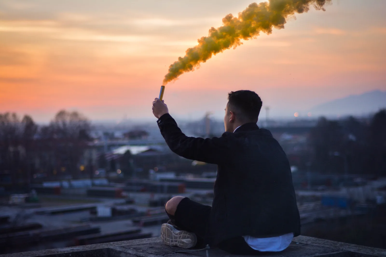 Pessoa segurando um sinalizador de fumaça amarela em um terraço ao pôr do sol, representando a aura amarela